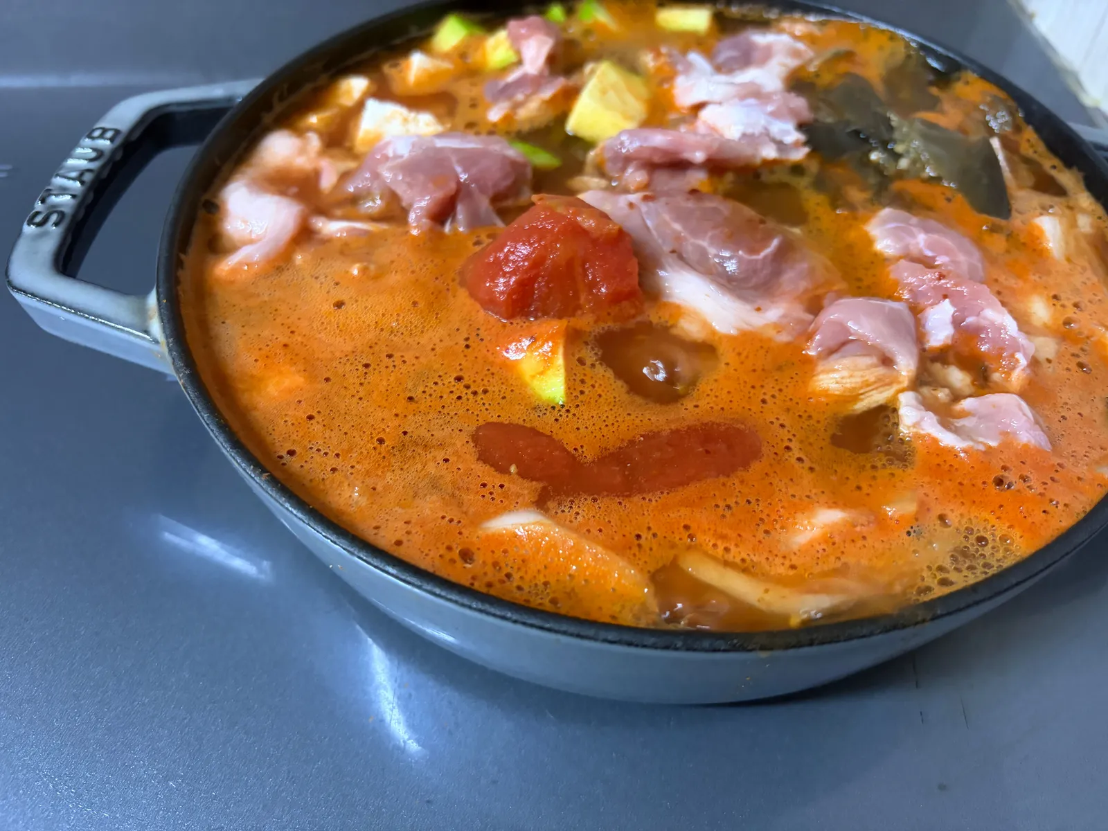 Kimchi jjigae coming to a simmer with pork slices and whole tomatoes in an orange-red broth