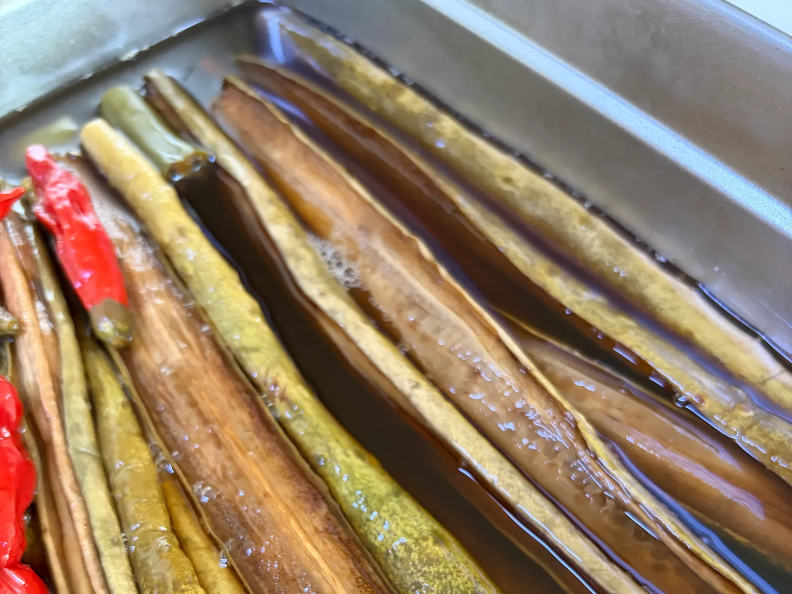 Whole Korean oiji cucumber pickles and red chili peppers sitting in brine in a metal container