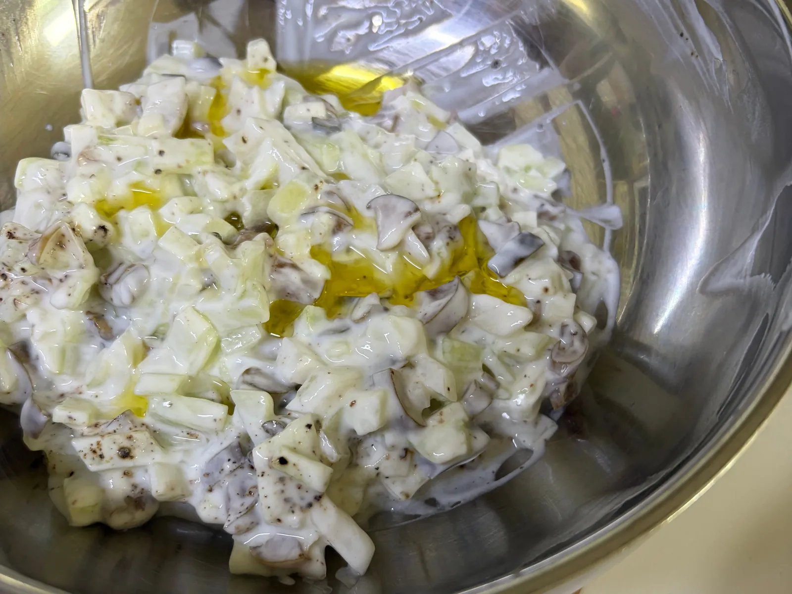 Diced Korean oiji cucumber pickles in plain yogurt with black pepper and a drizzle of olive oil in a steel bowl